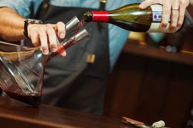 Şarap garsonu kırmızı şaraptan mükemmel bir renk elde etmek için cam sürahiye kırmızı şarap döküyor. Barda sürahisi olan bir erkek garson. Barmen tortuyu bozmadan şarabı sulandırıyor.