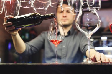 Barmen, barmen, barmen, tezgahta duran kırmızı alkollü bardaktan şarap bardağına kadar içki dolduran erkek. Barmen, garsonlar restoranda bardakları şarap şişesiyle dolduruyor..