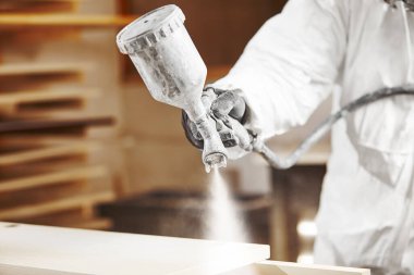 Boyalı sprey tabancayla çalışan, oduna havasız sprey sıkan bir adam. İşçi boyacıda solunum cihazı takıyor..