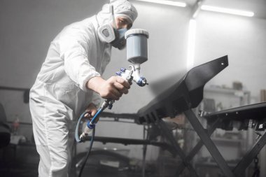 Tamirat sırasında arabanın siyah kısmına vernik kaplama parçaları püskürten oto tamircisi boya odasında sprey tabanca kullanıyor. Arabanın onarımı için servis. 