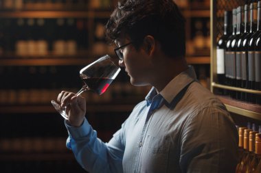 Şarap dükkanında şarap tatma konusunda usta. Şarabın aromasını, tadını ve kalitesini değerlendirmek için şişelerin yanında duruyor..