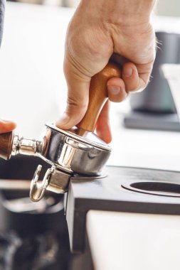 Yetenekli barista, kahve dükkanında espresso demlemeden önce liman filtresindeki kahve tellerini sıkıştırırken görülmüş..