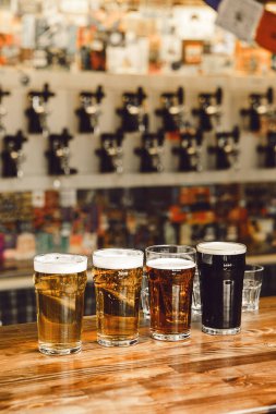 Dört farklı bardakta bira, ahşap bar kapağında, çeşitli renkler ve sınıflandırma tarzları sergileniyor..