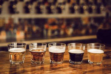 Farklı bira stilleriyle dolu beş küçük bardak seti ahşap bardakta düzenlenir. Her bardak farklı renk ve doku, davetkar tatma ve karşılaştırma sergiler.