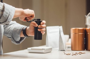 Baristaların elleri, kahve çekirdeklerini manuel kahve tezgahının üstünde titizlikle öğütüyor. Taze fasulyeler yakınlarda serpilmiş, ve teneke kutular ve ölçekler hazırlıkta hassasiyet olduğunu gösteriyor..