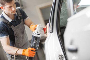 Adam oto tamirhanesinde beyaz araba cilalıyor, yakın plan. Yörünge cilası makinesi. Cilalı bitiş. Otomobil kaportası ayrıntıları.