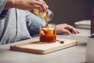 Kişi, taze demlenmiş kahveyi küçük sürahisinden, tahta kesme tahtasındaki buz küpleriyle dolu bardağa döker ve buzlu bir Americano yaratır.. 
