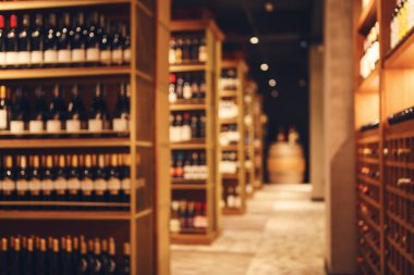 Şarap dükkanındaki büyük mahzende alkollü içecekler için ahşap raflar. Seçkin alkollü içeceklerle dolu uzun şarap koleksiyonu koridoru. Şarap dükkanının mahzeninde çeşitli şişelerle raflar..