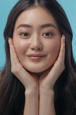 Çekici bir Japon şehvetli genç kadının güzel ön portresi. Temiz tenli ve uzun esmer saçlı. Yüzüne dokunuyor. Cilt bakımı, kozmetoloji ve plastik