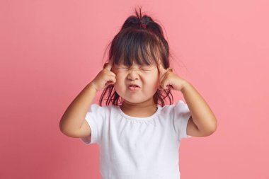 Ciddi küçük Asyalı etnik kızın portresi, önemli bir şeyi hatırlamak için parmaklarını şakaklarda tutar ve gözlerini kapatır. Pembe tişörtün üzerinde tek başına duran beyaz tişört giyer.