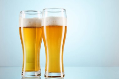 Sarı alkollü gazlı içecek, arka planda şişirmek için bardakları dolduruyor. Bira, iki bardakta köpüklü bira. Bira listesi, menü şablonu, afiş, afiş, poster, reklam. Mesaj için yer. Yan görünüm.