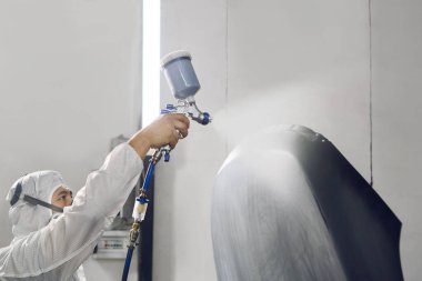 Oto tamircisi, tamirat sırasında boya odasına sprey tabancayla siyah araba parçalarını boyayıp cilalıyor. Arabanın onarımı için servis. 