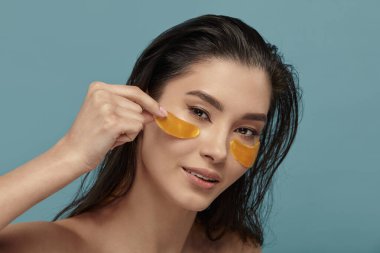 Güzel kız yüzüne altın hidrojel bantlar takıyor. Göz maskesi altında su içen mutlu bir kadın. Güzellik ürünleri, kozmetik ürünleri, yaşlanma karşıtı kadın prosedürleri, cilt bakımı. Yakın çekim..