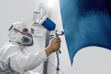 Profesyonel erkek araba boyacısı arabayı boyayarak boyuyor. Garajda boyayla maviye boyuyor. Adam sprey tabancayla çalışıyor. Vücut tamir arabaları.