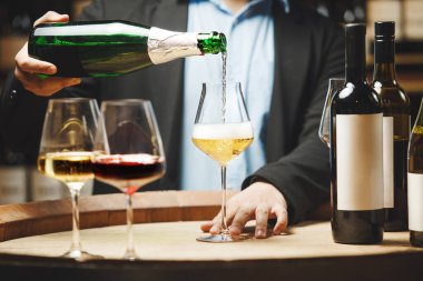 Klasik takım elbiseli şarap garsonları mahzendeki şarap tatma sırasında bardağa köpüklü şarap dökerler ve masada başka bardaklar da vardır..