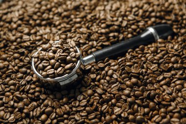 Paslanmaz çelik espresso portafilteri ağzına kadar taze kavrulmuş kahve çekirdekleri ile doldurulur, diğer fasulyelerin yatağında dinlenir, yakın plan..