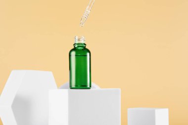 Boynunda pipet kapağı olan açık yeşil damlacıklı mini şişe, sarı arka planda beyaz geometrik şekillerle çevrili küp üzerinde duruyor. Uzayı kopyala Güzellik ürünleri pankartı, şablon.