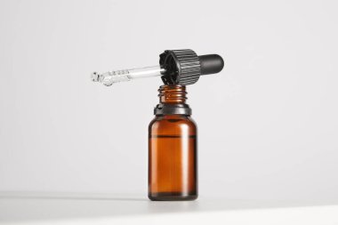 Pipetli siyah başlık açık kahverengi cam üzerinde duruyor. Tıbbi, kozmetik veya kimya endüstrisi için küçük bir şişe. Kehribar şişesi, kap, güzellik ürünü ambalajı, şeffaf sıvıyla birlikte. Metin için yer.