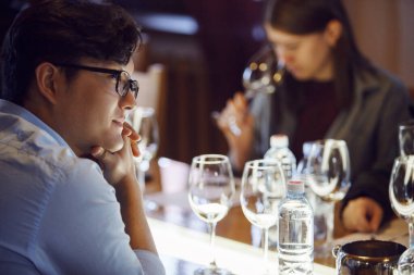 Gözlüklü Asyalı şarap garsonu şarap kadehleriyle çevrili şarap okulunu dikkatle dinlerken, katılımcı da şarap aromasını değerlendiriyor.. 