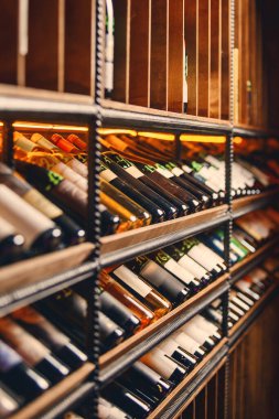Parlayan ışıkları ve ahşap bölmeleri olan uzun bir şarap rafının dikey görüntüsü. Zarif bir depoda şarap şişeleri sergileniyor..
