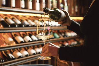 Şarap mahzeninde sıcak bir şarap mahzeninde bir şarap garsonunun tuttuğu bir bardağa akan beyaz şarap yakın plan..