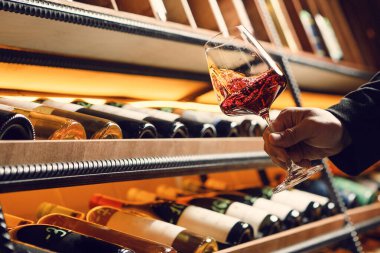 Kiler raflarının yanında duran temiz bir bardakta dönen kırmızı şarabın yakın çekimi zarif bir hareket ve şarap gövdesini yakalıyor..