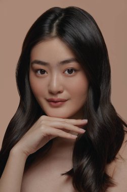 Yüzüne bej bir arka planda dokunan sağlıklı bir cilde sahip güzel Asyalı kadın modelinin dikey yakın portresi. Yüz bakımı, yüz bakımı, kozmetoloji, güzellik ve kaplıca, Asyalı kadınlar