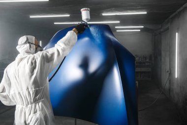 Profesyonel kaporta işi, koruyucu maskeli ve iş kıyafetli erkek araba boyacısı sprey tabancadan otopark kabinine birkaç kat boya sür. Boya odasında araba boyama