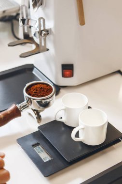 İki boş espresso fincanı dijital ölçekte otururken, portafilter yakınlarda kahve makinesinde demlenmeye hazır bir şekilde duruyor. Profesyonel espresso yapma becerisi..