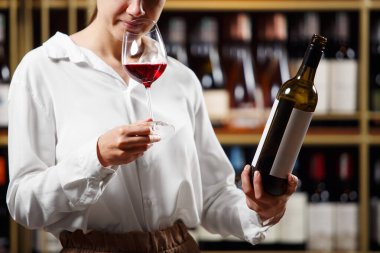 Şarap mahzeninde şarap içen genç ve güzel bir şarap garsonu, yakın çekim fotoğrafı. Alkollü içecekler degulasyonu. Şarap yapma okulu, şarap garsonu sertifikası. Profesyonel Dernek