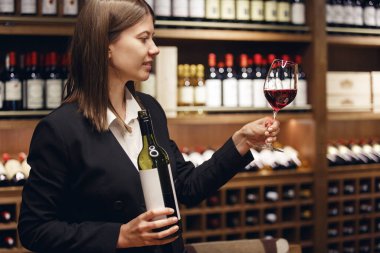 Tecrübeli kadın şarap garsonunun mahzende şarap tadıp arka planda duran şarap kadehinin kapalı bir portresi. Farklı şaraplar üzerinde çalışmak için şarap garsonluğu sınavı. Profesyonel şarap yapma eğitimi.