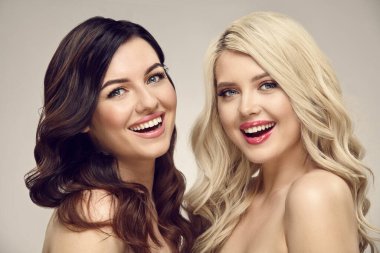 İki gülümseyen esmer ve temiz tenli, güzel dalgalı saçlı sarışın kadının stüdyo fotoğrafı..