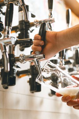 Barmen ustalıkla bardaktan bardağa altın bira doldurur. Kalabalık bar atmosferi gevezelikle doludur ve müşteriler içkilerinin keyfini çıkarırken bardaklar tıkırdar..