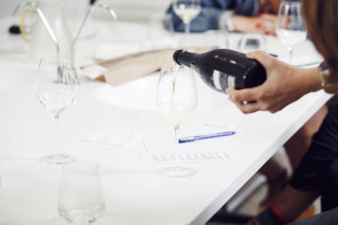 Antrenman sırasında şarap bardağına beyaz köpüklü şarap dolduran şarap garsonunun yakın çekimi. Eğitim ve şarap tatma..