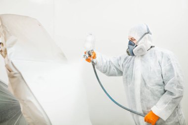 İşçi arabaya beyaz boya püskürtüyor. Boya kabininde profesyonel bir araç resmi.