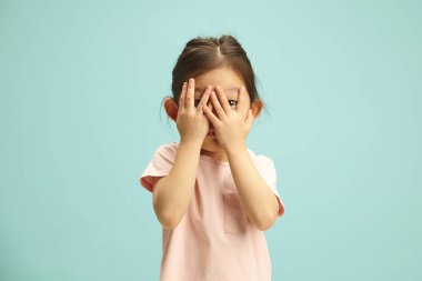 Korkulu Asyalı etnik kökenli bir kızın izole edilmiş bir portresi. Beş yaşındaki küçük kız korkuyla gözlerini kapatıyor. Endişe verici bir şekilde parmaklarının arasından izliyor. Çocuk