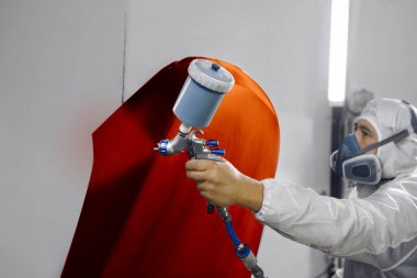 Araba spreyi boyacısı, endüstriyel bölmedeki sprey tabancadan kırmızı boya püskürtüyor. Arabanın onarımı için servis. 