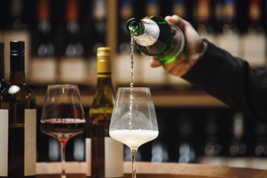 Şarap şişesinden cama köpüklü şarap döken, şarap mahzeninde şarap şişeleriyle kaplanmış, tanınmayan profesyonel şarap garsonunun el çekimi.. 