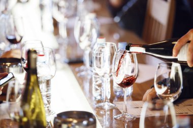 Garson şarap yarışması sırasında şarap kadehlerine kırmızı şarap koyuyor. Alkollü içecekler için şarap garsonu ve personel eğitimi. Profesyonel iş sertifikası sınavı. Şarap.