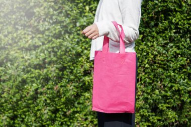 Pembe bir çanta tutuyor. Yeniden kullanılabilir ve çevre dostu yaşam tarzı seçimleriyle sürdürülebilirliği teşvik etmek.