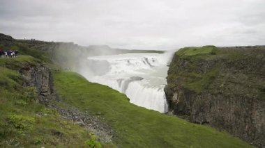 İzlanda 'daki güçlü Gullfoss şelalesini görüntüleyen video, turistlerin manzaralı uçurumlardan izlediği bir görüntü. Şelale sularından yükselen sis yemyeşil kanyonda dramatik bir atmosfer yaratıyor..