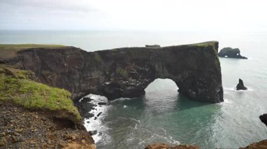 İzlanda 'daki devasa Dyrhlaey kaya kemerinin altında dalgaların çarpışını gösteren yavaş çekim videosu. Engebeli uçurum ve dönen okyanus bu ikonik kıyı işaretinin çarpıcı güzelliğini vurguluyor..