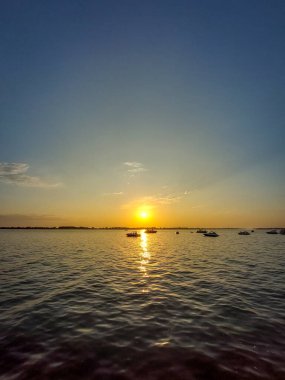Gün batımı, uzaktaki teknelerle sakin sulara yansıyarak denizdeki huzur ve tefekkürün altın bir sahnesini oluşturdu..