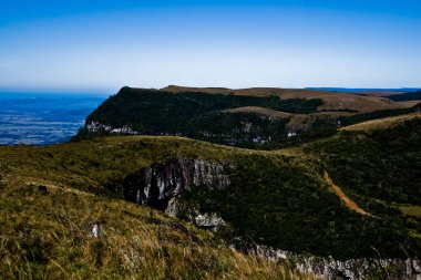 Yerli bitki örtüsüyle kaplı, arka planda mavi bir gökyüzü olan dağlık bir platonun panoramik görüntüsü.