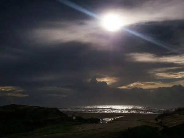 Deniz kenarı sahnesi şafak vakti karamsar bir gökyüzü ve yoğun bir ışık okyanusa yansıyor, gizem ve tefekkür çağrıştırıyor..