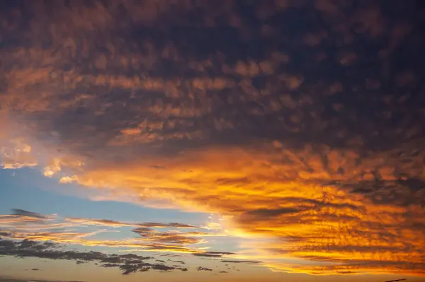 Gökyüzü koyu altın ve turuncu tonlarda desenli bulutlarla dolu. Alacakaranlıkta ufukta açık mavi bir iz var..