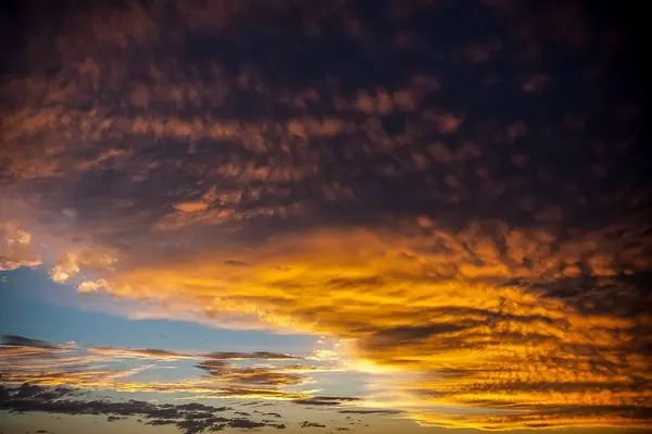 Parlak gökyüzü, gün batımında mavi ufuk ile çelişen altın ve turuncu tonlarda desenli bulutlar..