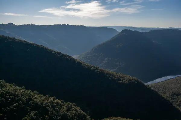 Dağlar bitki örtüsüyle kaplı, açık mavi gökyüzünün altında birkaç bulutla doğal katmanlar oluşturuyor..
