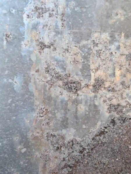 Paslı ve oksitlenmiş bölgelerin yer aldığı, yanardöner yamalı gri ve kahverengi renkler gösteren, aşınma detaylarını ve küçük pas parçalarını vurgulayan eski bir metal yüzeye yakın plan..