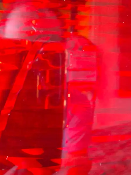 Yayılmış ışık yansımaları ile yarı saydam kırmızı bir yüzeye yakın çekim, dikey çizgiler ve soyut derinlik hissi uyandıran dalgalı desenler.